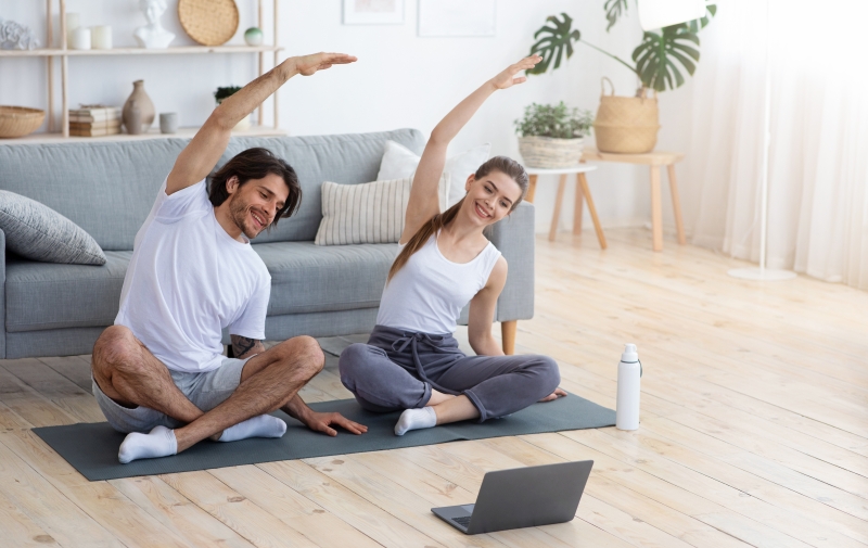 Healthy couple exercising at home, sitting on sport mat and watching videos on laptop, copy space